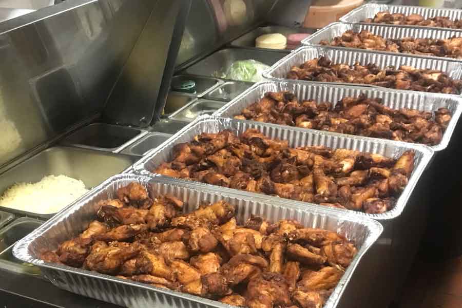 Large buffalo wings catering order in six catering party trays on counter being made