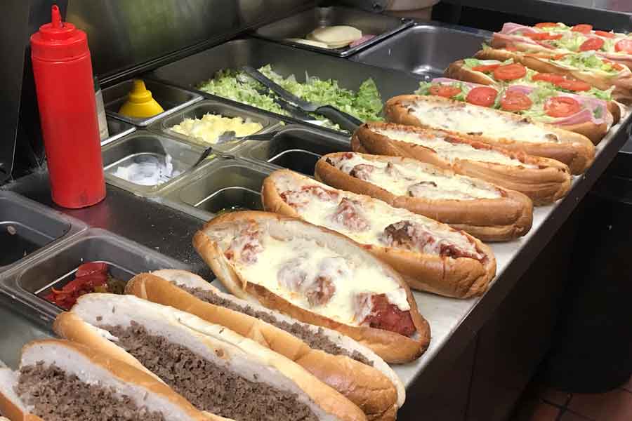 Steak sandwiches, hoagies, meatball parmigiana sandwiches in a row on the counter